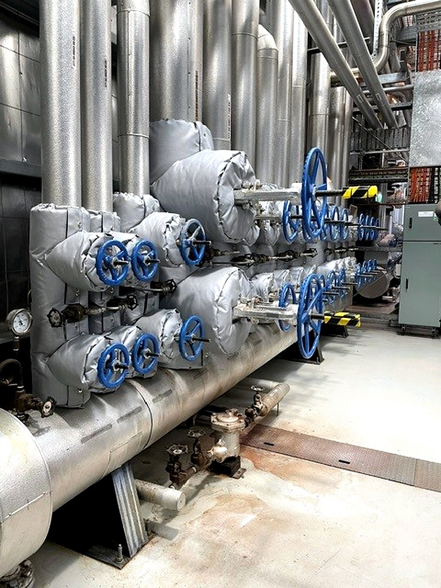 Multiple thermal jackets on blue-handled valve assemblies on a large hot water distribution manifold